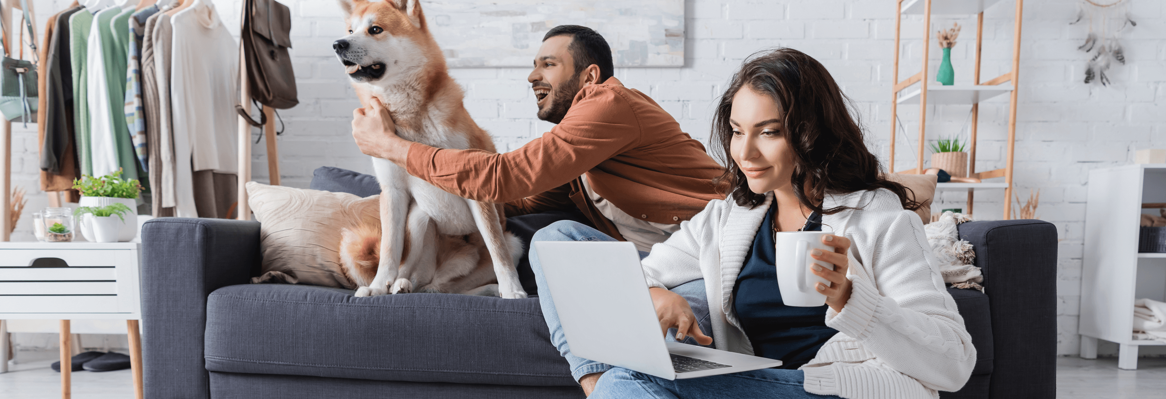 Paar mit Laptop und Hund in einem hellen Wohnzimmer